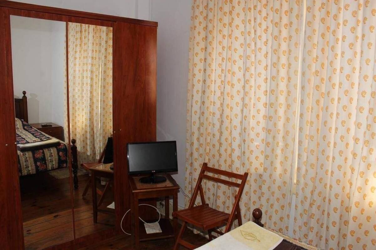 Ein Zimmer mit einem Bett, einem Schreibtisch mit Computer, einem Stuhl und einem Fernseher.