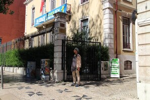 A man standing in front of a building with a blue sign that reads "VIVER SEM" and a white sign that says "CASA DE CAMPO". - Viriato Rooms (Lisbon)