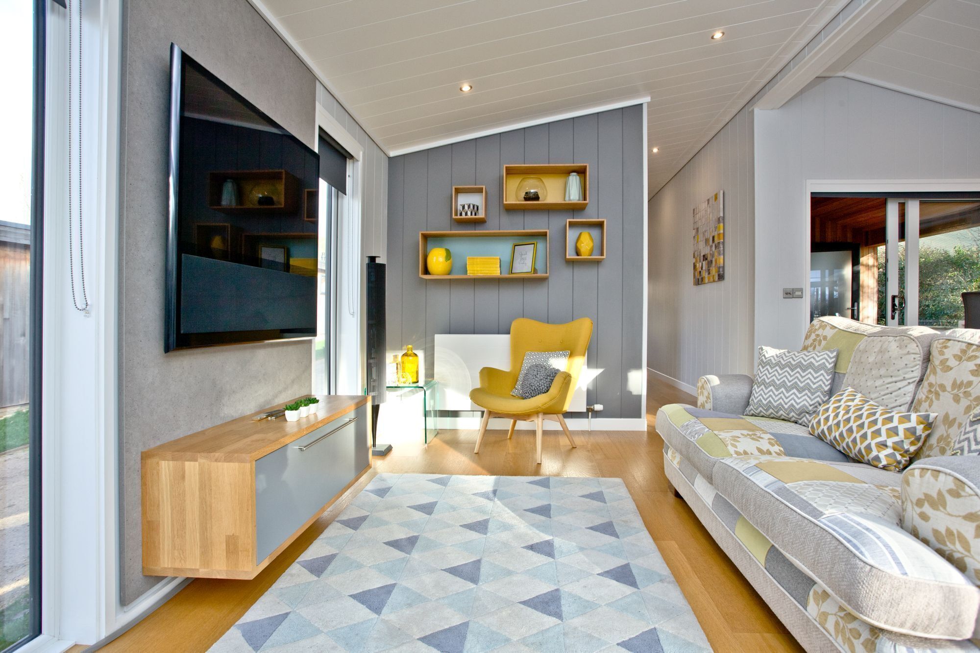 Ein modernes Wohnzimmer mit einer Couch, einem gelben Sessel und einem an der Wand montierten Fernseher.