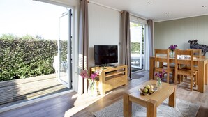 Een ruime woonkamer met een grote televisie, houten meubels en uitzicht op groen.