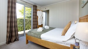Een slaapkamer met een houten bed, wit beddengoed, een groene plaid en uitzicht op groen buiten.