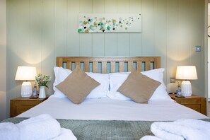 A neatly made bed with two pillows, a wooden headboard, and two bedside tables with lamps and a vase of flowers. - Whileaway Lodge, Hot Tub, Wi-Fi (Cheddar)