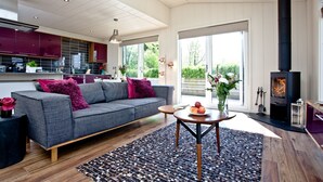 A modern living room with a grey sofa, a round wooden table, and a black fireplace. - Mulberry Lodge, Strawberryfield Park (Cheddar)