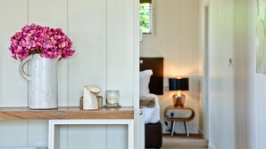 A hallway with a white door, a bed with a white headboard, and a small table with a lamp. - Mulberry Lodge, Strawberryfield Park (Cheddar)