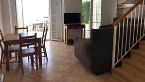 Un amplio salón con una mesa y sillas de madera, un sofá, un televisor y una escalera.
