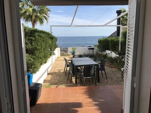 An outdoor patio with a table and chairs, a view of the sea, and a white railing.
