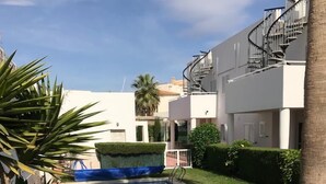 Una piscina rodeada de césped cuidado y palmeras, con un edificio moderno al fondo.