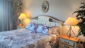 Un dormitorio con cama, dos mesitas de noche, un tocador, un espejo y una planta en maceta.
