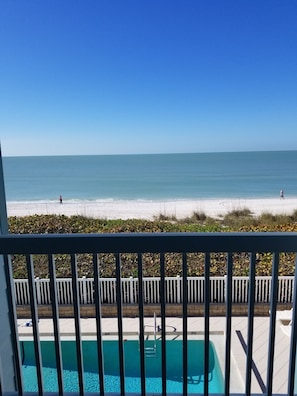 A balcony with a view of a beach and a swimming pool.