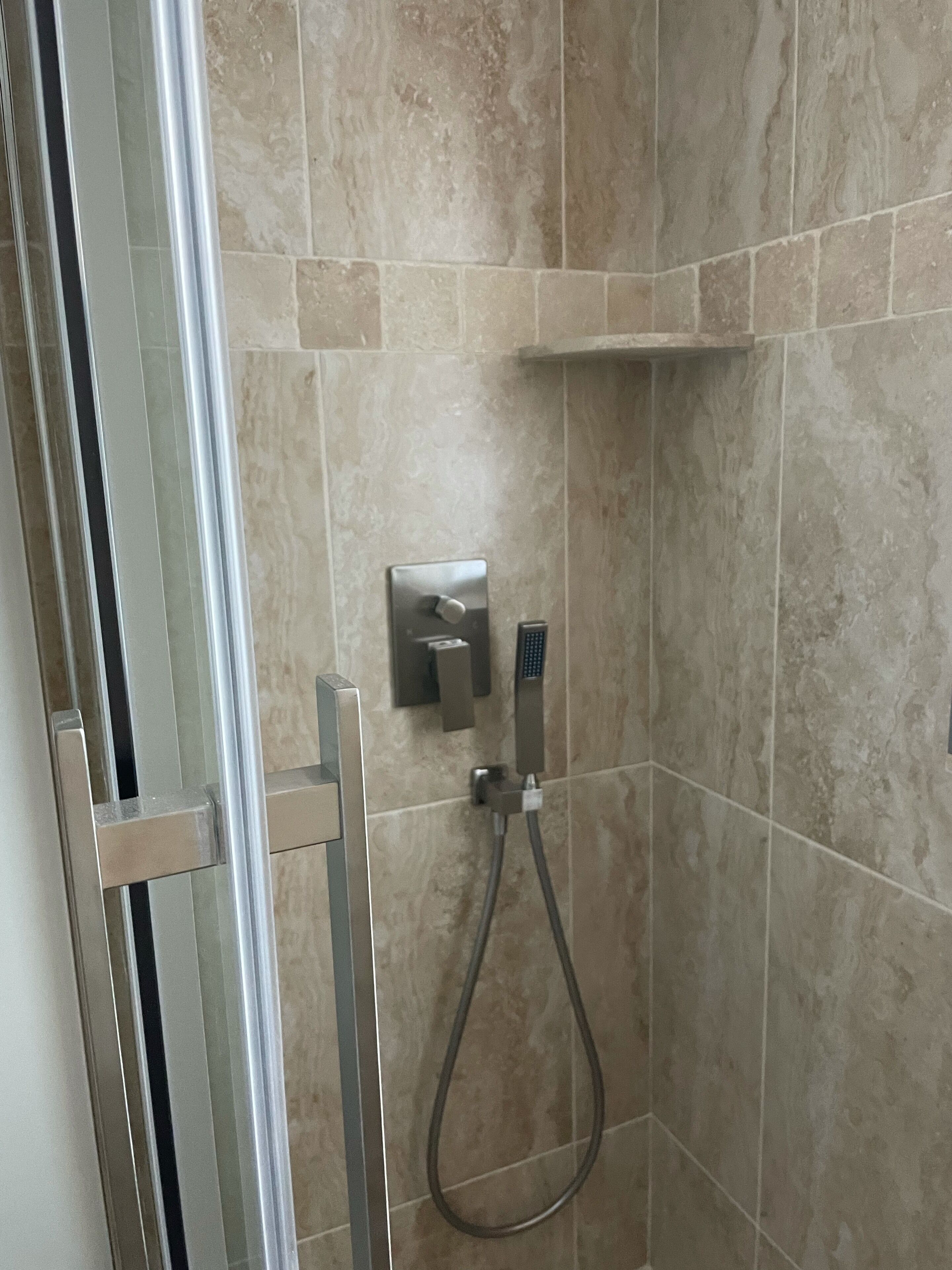 Une douche équipée d’un pommeau de douche à main et d’un panneau de commande fixé au mur.