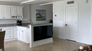 A modern kitchen with white cabinets, a black range hood, and a painting of a tropical scene. - Marco Island Riverside Condo - Comfort Meets Coastal Charm (Marco Island)