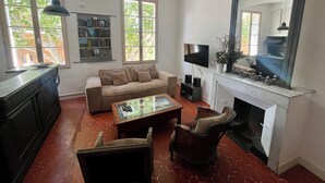 Ein Wohnzimmer mit Sofa, Couchtisch, Sessel, Kamin, Fernseher und Bücherregalen.