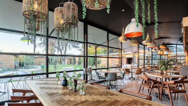 A spacious dining area with large windows, wooden tables, and hanging wicker lamps. - Droombos (Windhoek)