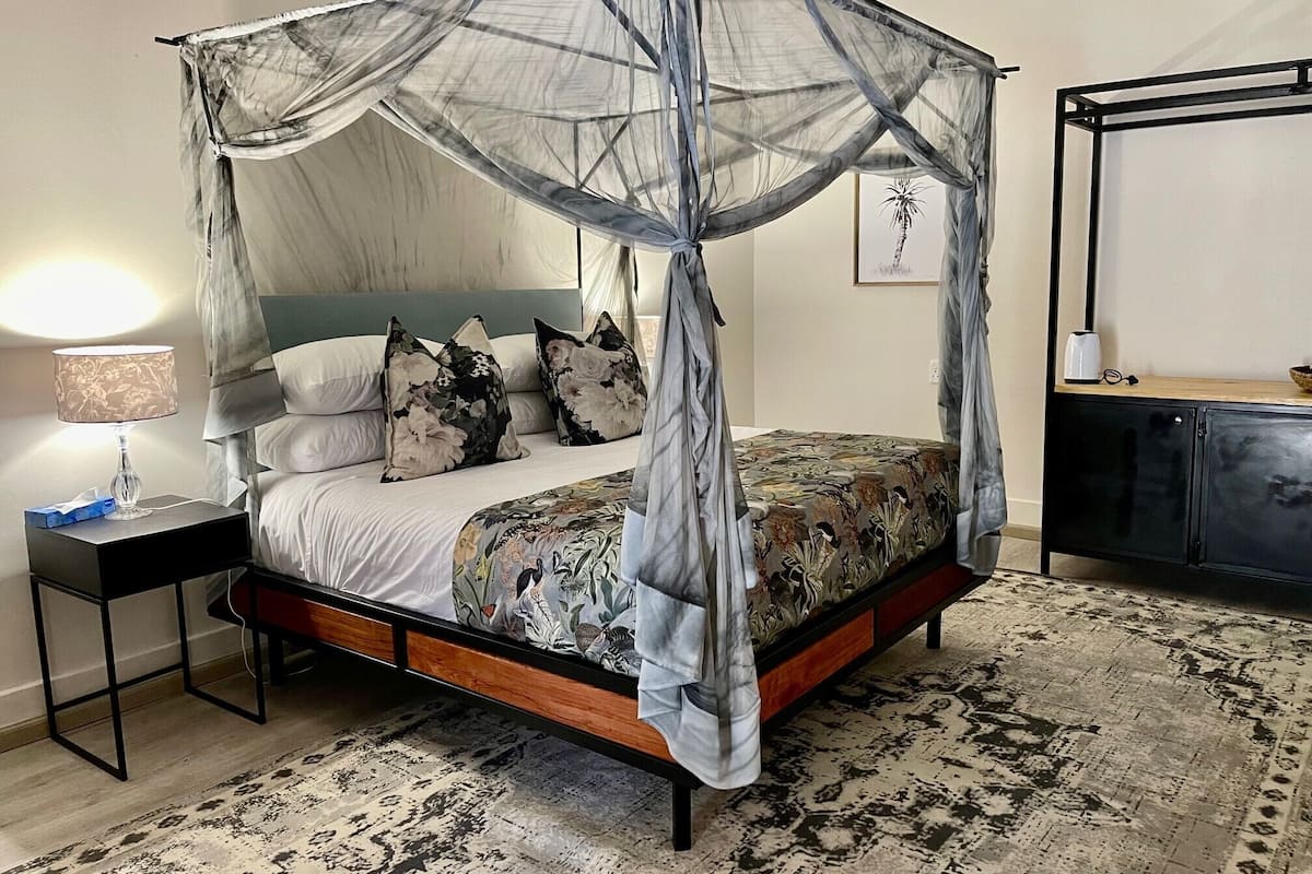 A four-poster canopy bed with floral bedding, a bedside table with a lamp, and a patterned rug.