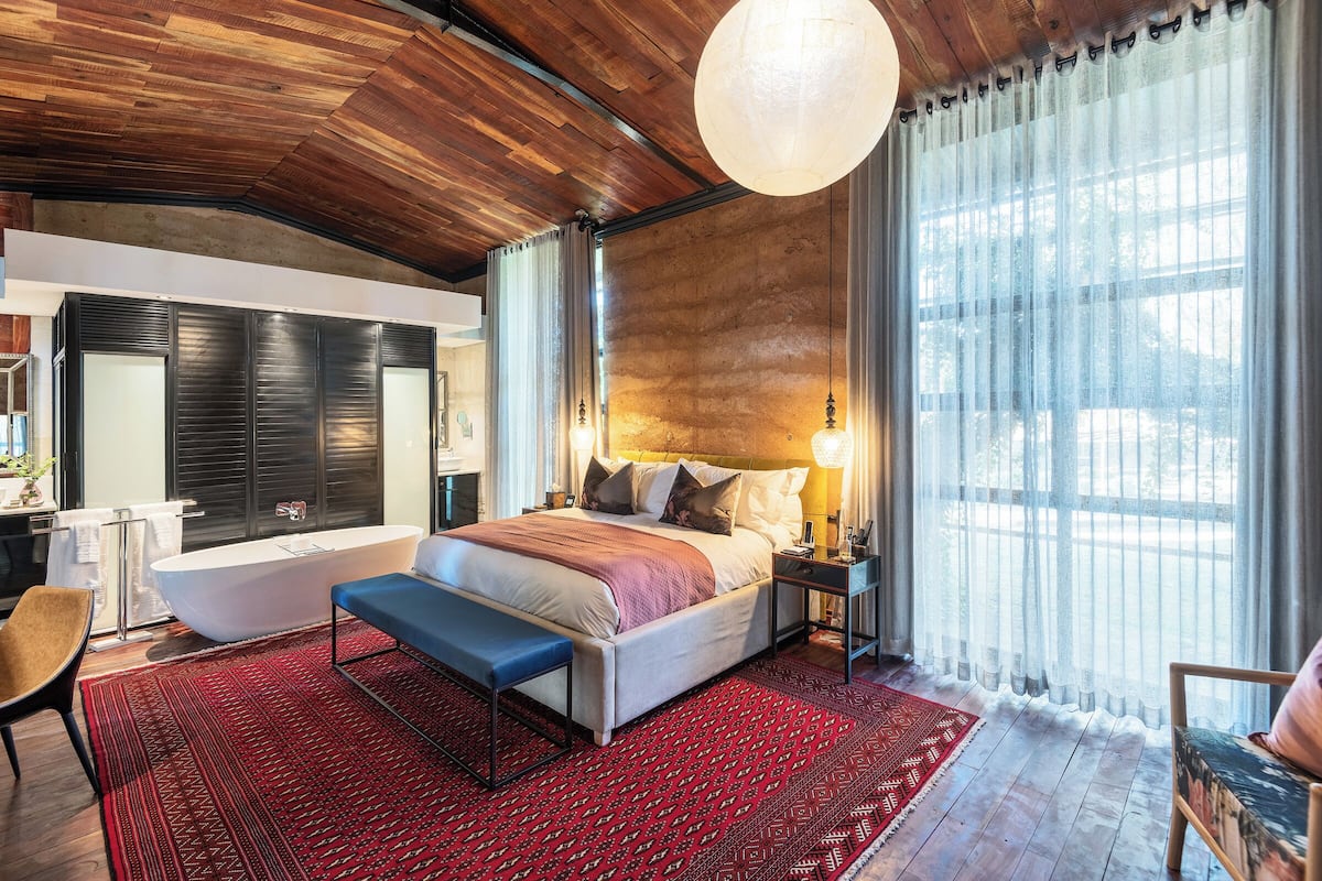 A modern bedroom with a large bed, a bench, a bathtub, and a view of the outdoors.