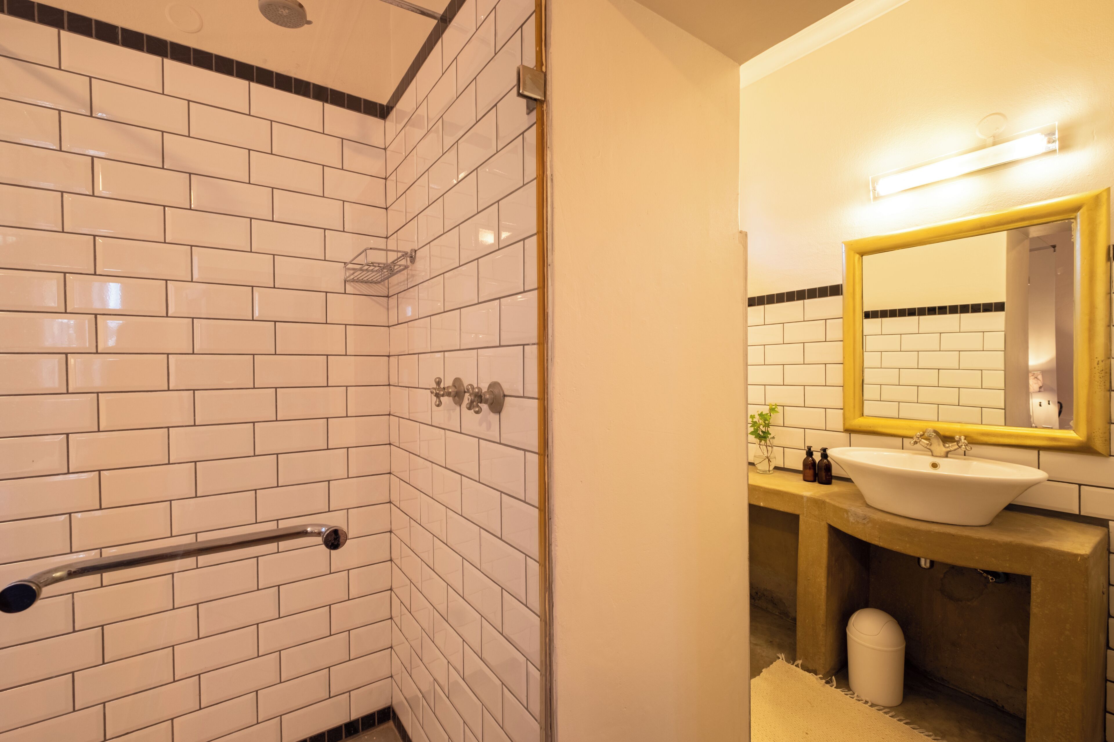 Un baño con azulejos blancos tipo metro, un espejo con marco amarillo, un lavabo y un perchero para toallas.