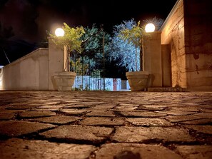 Un patio empedrado con una reja de metal, plantas en macetas y la fachada de un edificio.