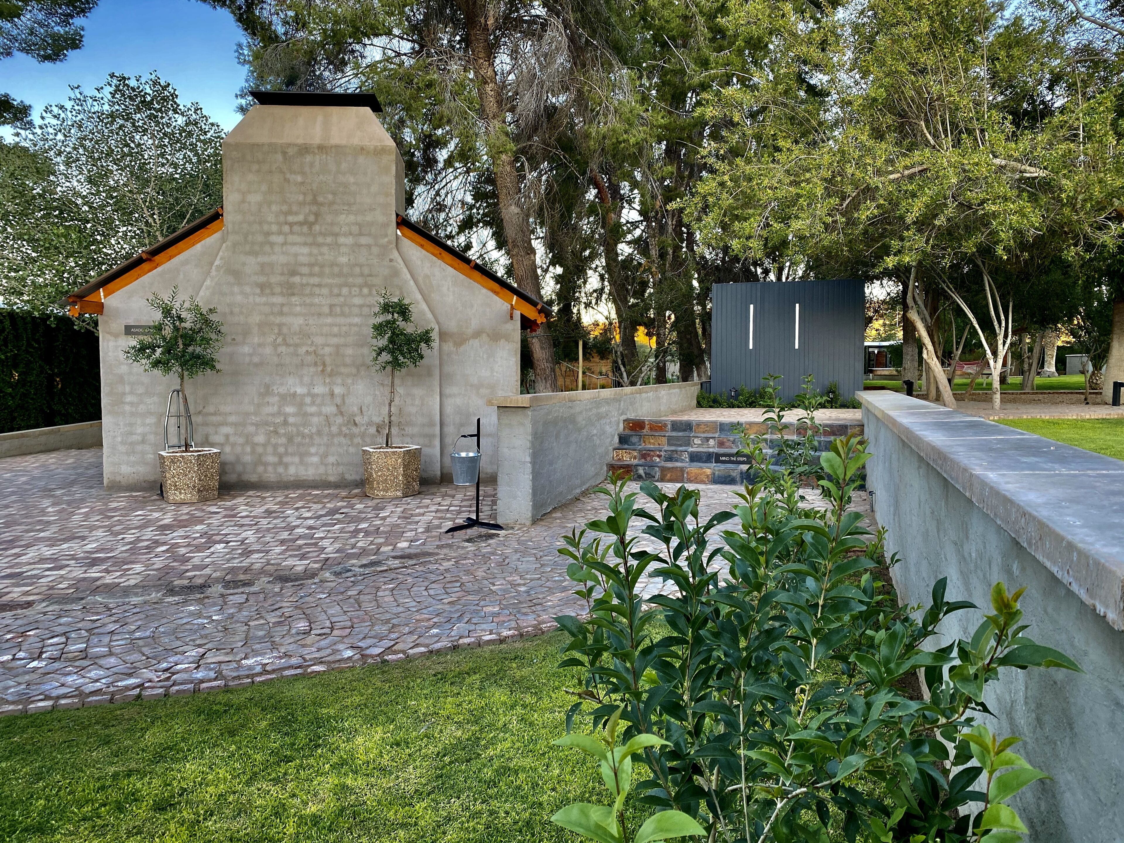 A patio area with a stone floor, a concrete wall, and a small brick structure with a metal roof.