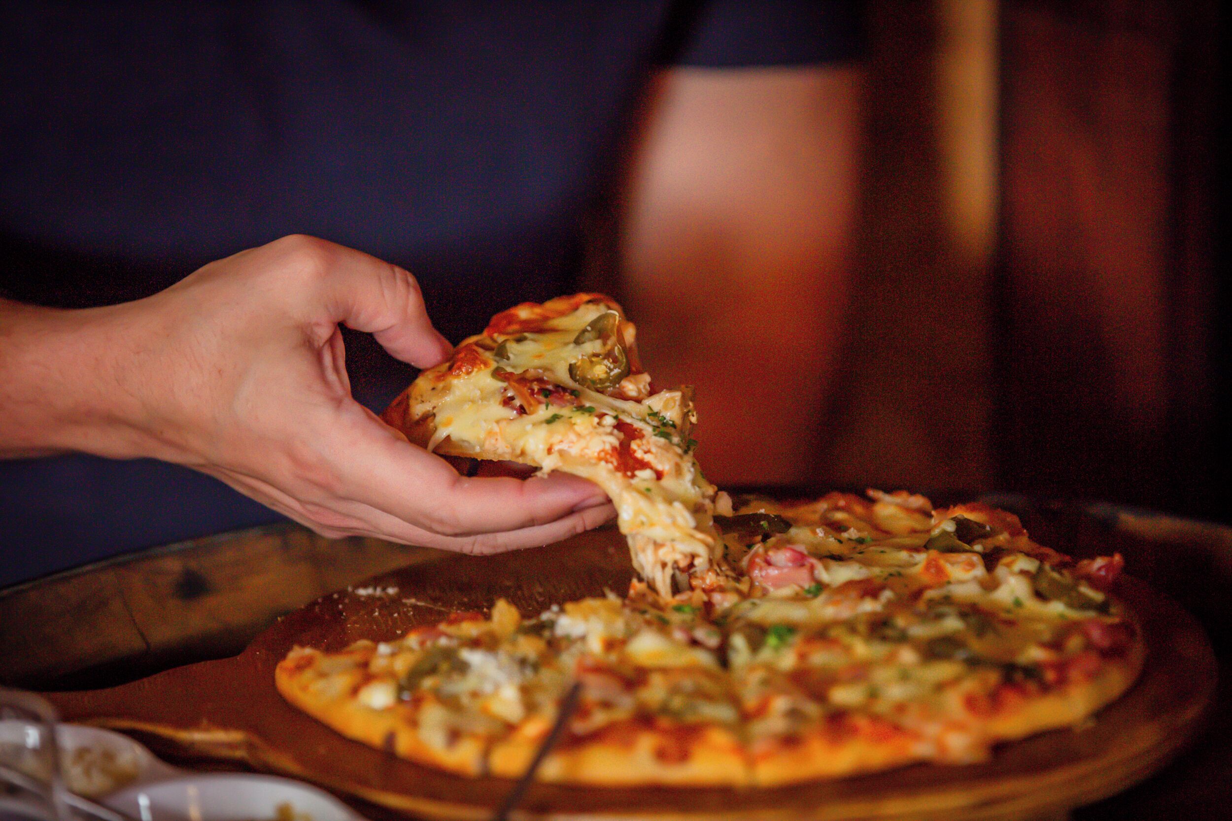 A person holding a slice of pizza with various toppings.