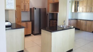 Eine Küche mit Holzausstattung, einem Edelstahl-Kühlschrank, einer Spüle und einer Kochinsel mit schwarzer Arbeitsplatte.