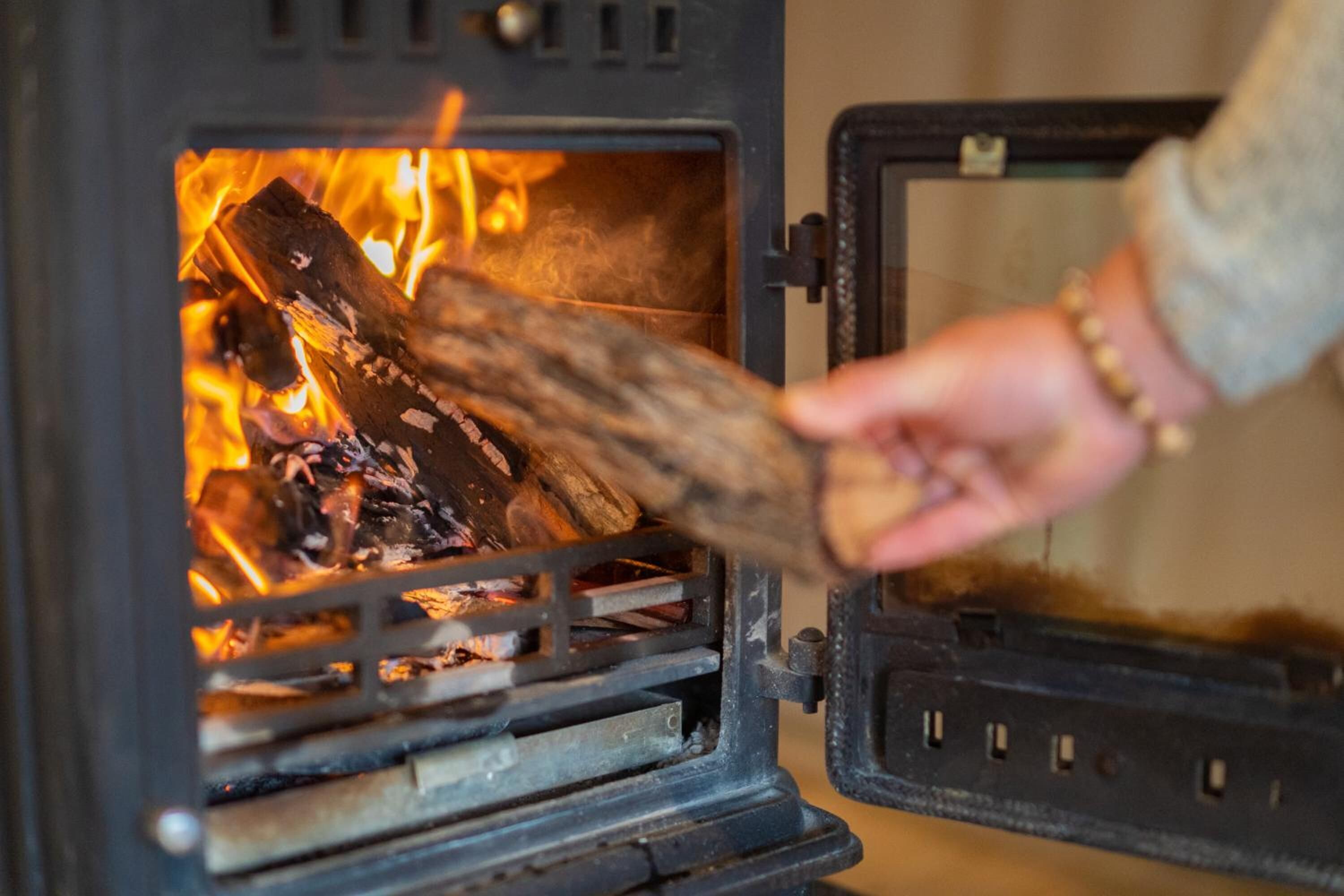 A person adding wood to a wood-burning stove.