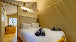 Uma cama de solteiro com lençóis brancos, um banco de madeira com almofadas e uma estrutura semelhante a uma tenda com um candeeiro.