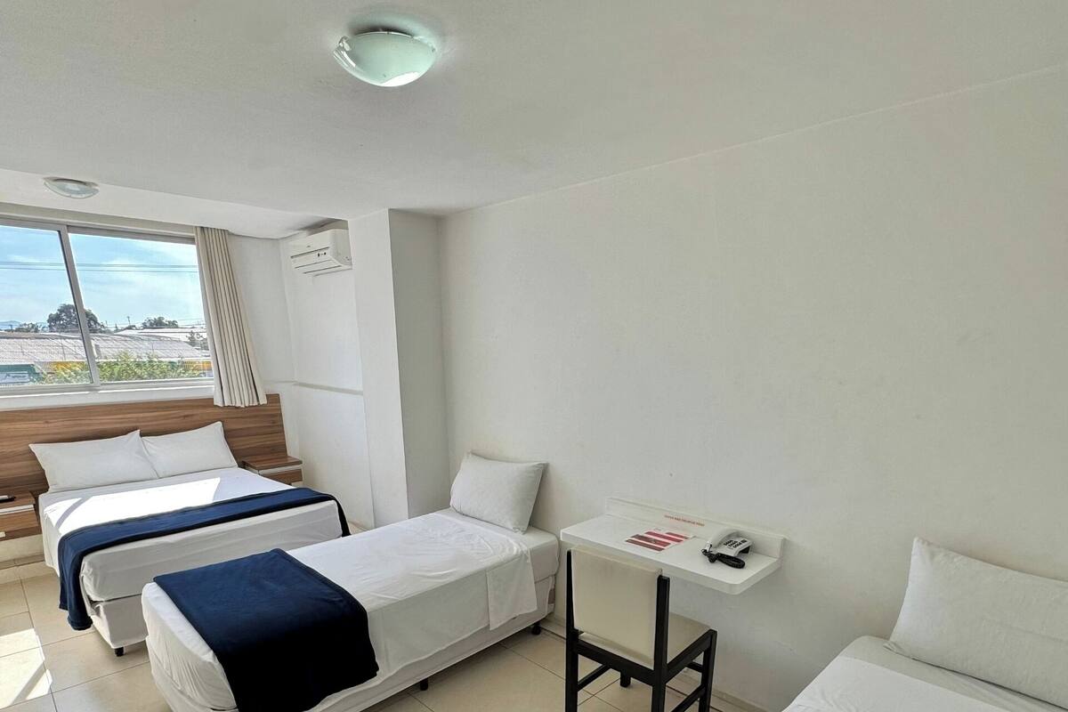 Hotellihuone, jossa on kaksi erillistä sänkyä, pieni pöytä, jossa on puhelin, ja ikkuna, jossa on verhot.
