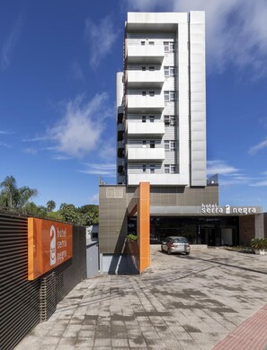 A modern hotel building with a prominent entrance, a parking area, and a clear sky. - Hotel Serra Negra (Betim)