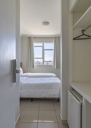 Una habitación de hotel con dos camas, una ventana con cortinas, un radiador y un perchero.