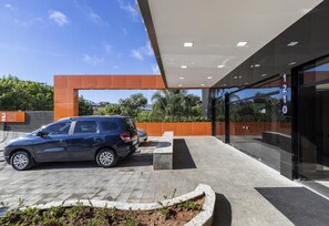 A modern hotel entrance with a car parked outside, a bench, and a clear sky. - Hotel Serra Negra (Betim)