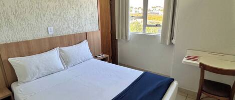 Habitación de hotel con una cama grande, cabecera de madera, mesita de noche, escritorio y ventana con cortinas.