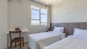 Habitación de hotel con dos camas, un escritorio con silla y ventana con vista a la ciudad.