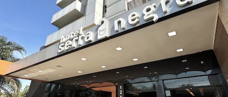 A hotel entrance with a modern facade, a visible address sign, and a landscaped area in front.