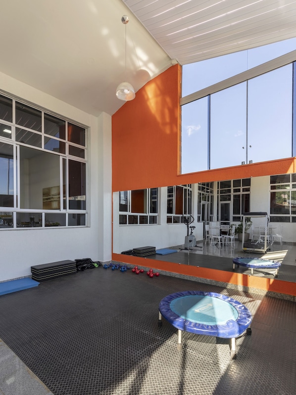 Un gimnasio con equipo de ejercicio, un trampolín y ventanas grandes.