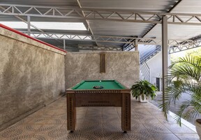 A pool table in a covered outdoor area with a concrete wall and metal beams.