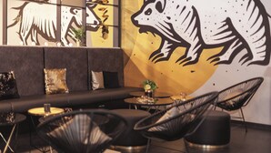 A modern lounge area with a sofa, round tables, and black chairs. A large wall mural depicts a stylized animal. - Holiday Inn - the niu, Coin Frankfurt Ostend by IHG (Frankfurt)