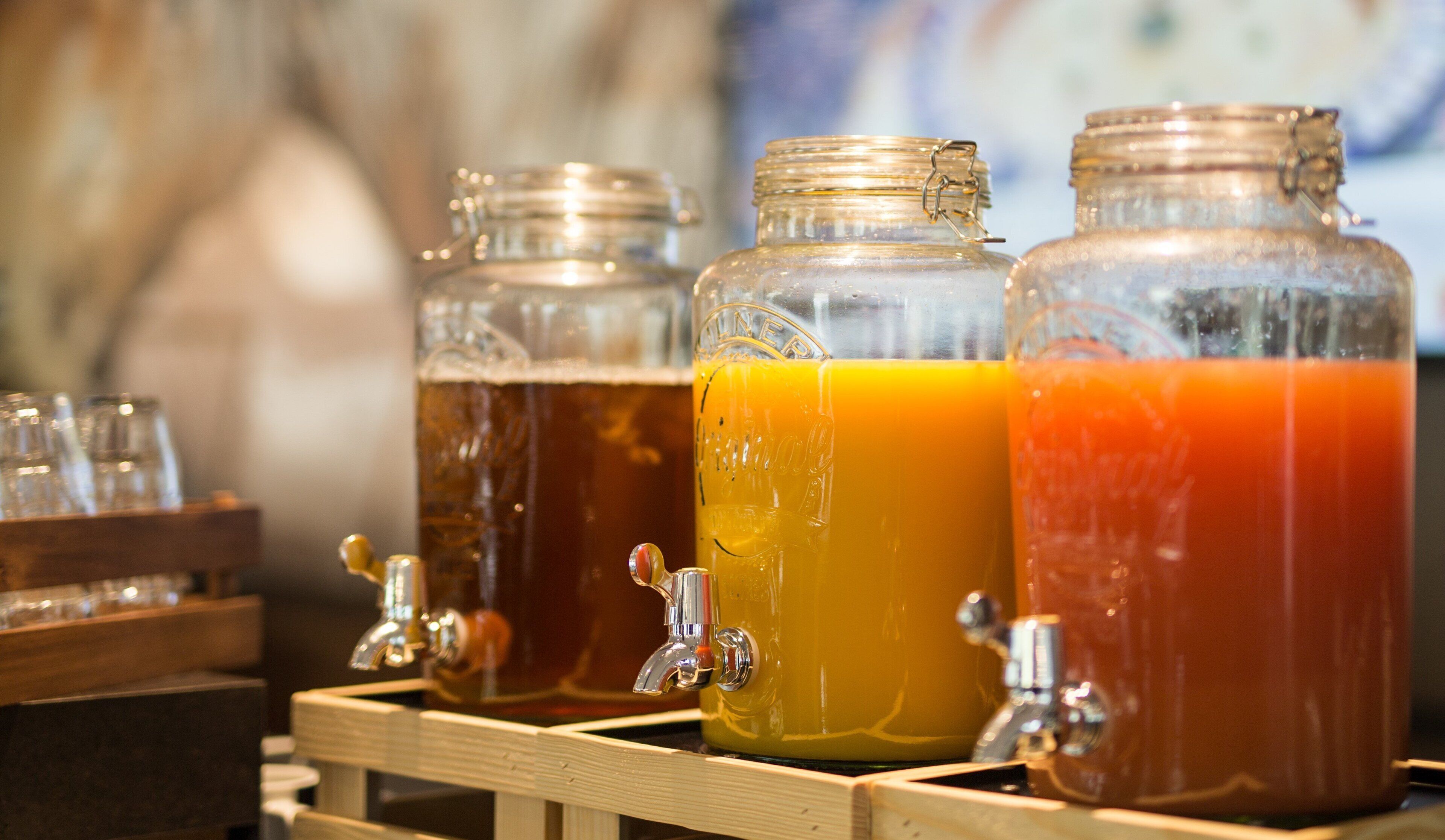 Three glass dispensers with taps, likely for beverages, on a wooden stand.