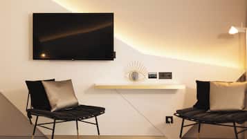 A modern room with a flat-screen TV mounted on the wall, two black leather chairs with cushions, a white shelf with decorative items, and a light fixture.