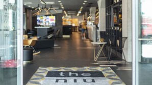 An interior view of a modern restaurant with a central counter, seating area, and a patterned floor leading to the entrance. - Holiday Inn - the niu, Coin Frankfurt Ostend by IHG (Frankfurt)
