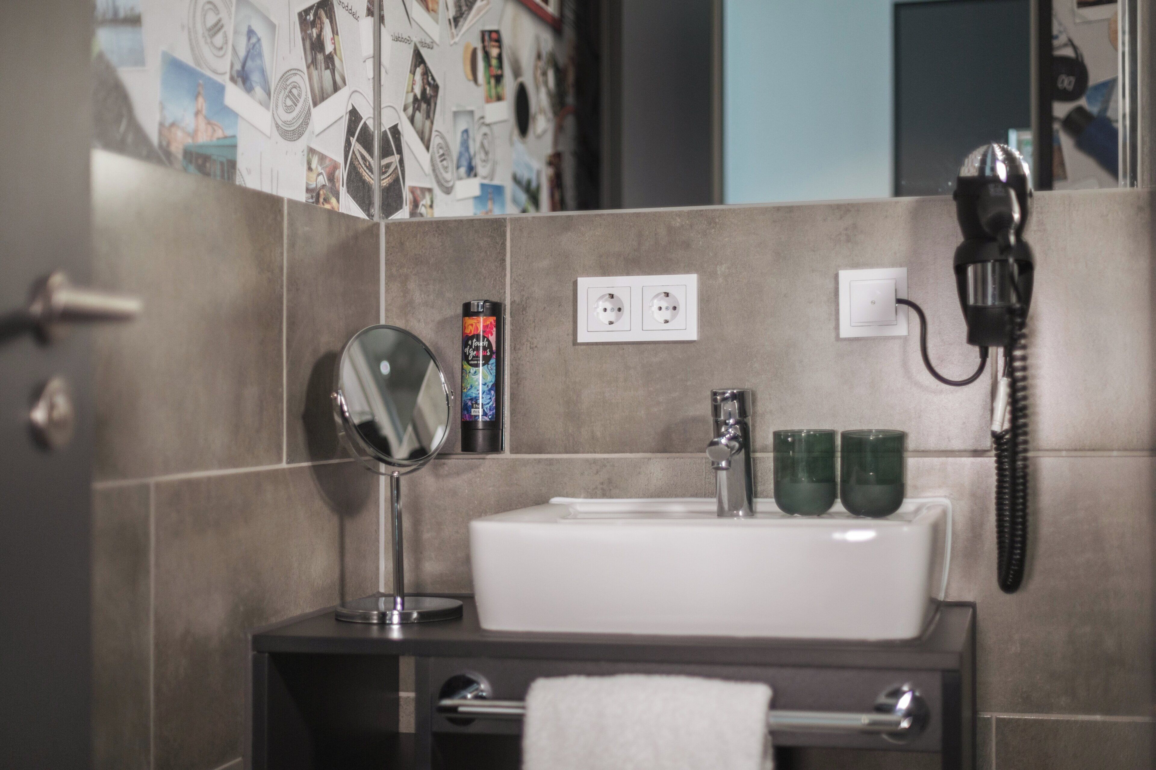 Une salle de bain avec un lavabo, un miroir et deux verres verts posés sur le comptoir.