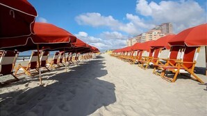 Uma praia com fileiras de guarda-sóis vermelhos e cadeiras de madeira.