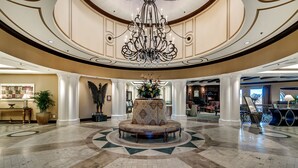 Um amplo saguão com área de estar circular central, um candelabro e piso de mármore.