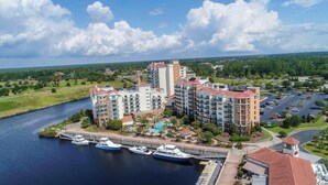 Um hotel na orla marítima, com vários edifícios, um cais e barcos, e uma área de estacionamento.
