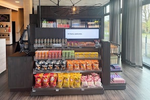 A snack display with various chips and snacks, a digital welcome message, and a view of the outside through large windows. - Holiday Inn - the niu, Air Frankfurt Messe by IHG (Frankfurt)