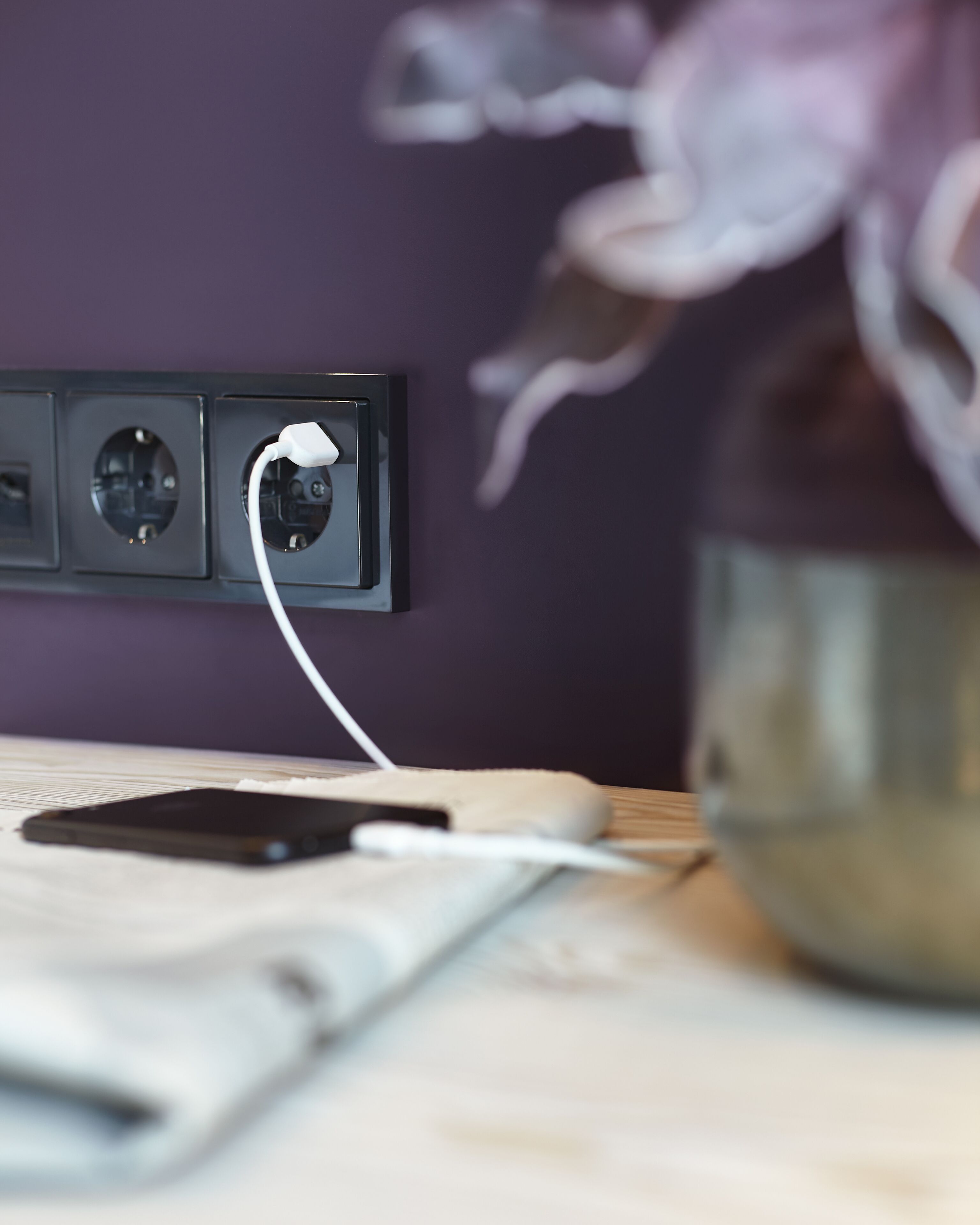 Primer plano de un enchufe de pared con un cable de carga blanco conectado a un teléfono inteligente.