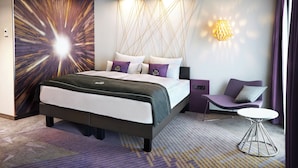 Ett modernt hotellrum med en stor säng, ett litet bord och en sittgrupp.