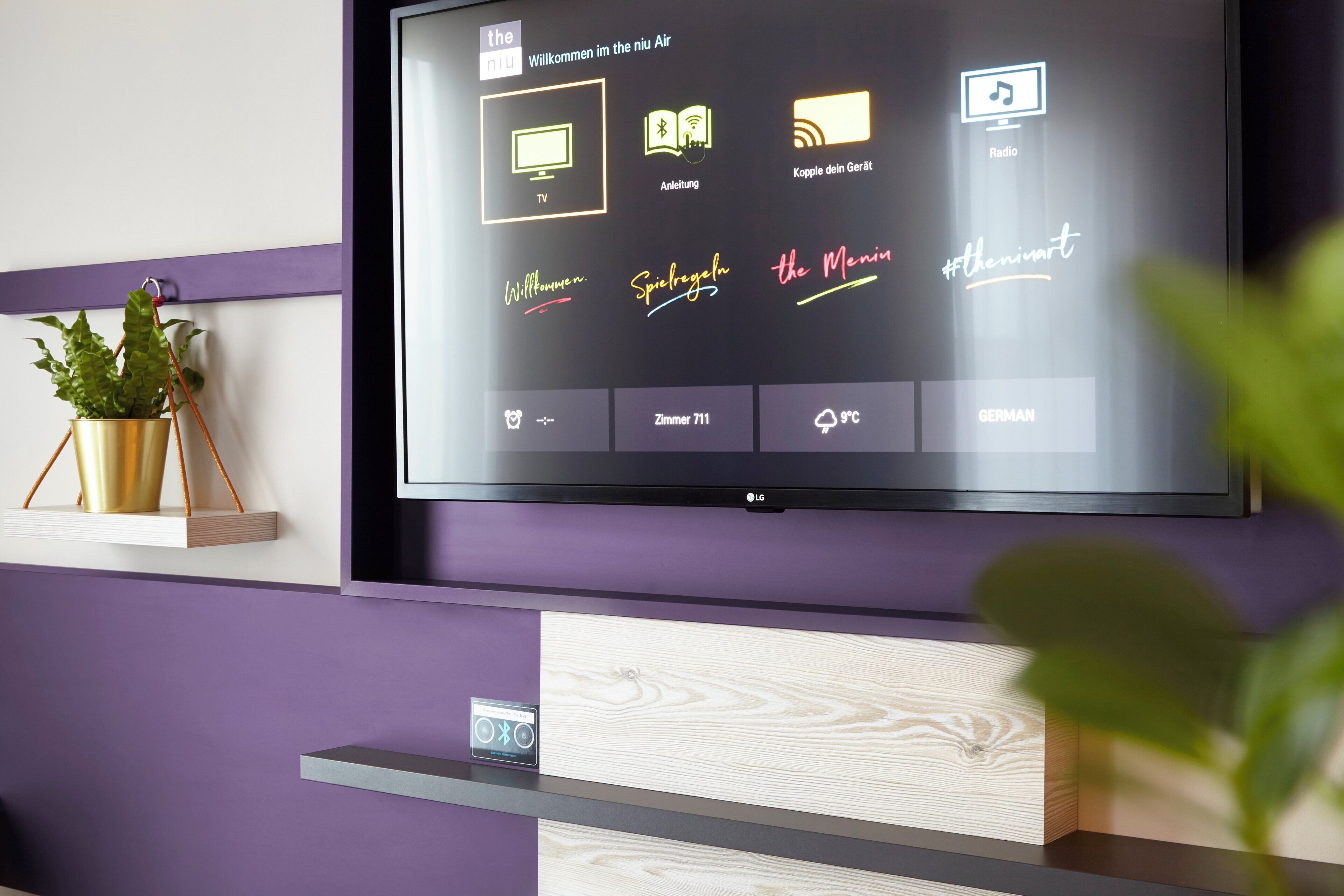 A television mounted on a wall with a purple and white color scheme, displaying a user interface with various icons and text.