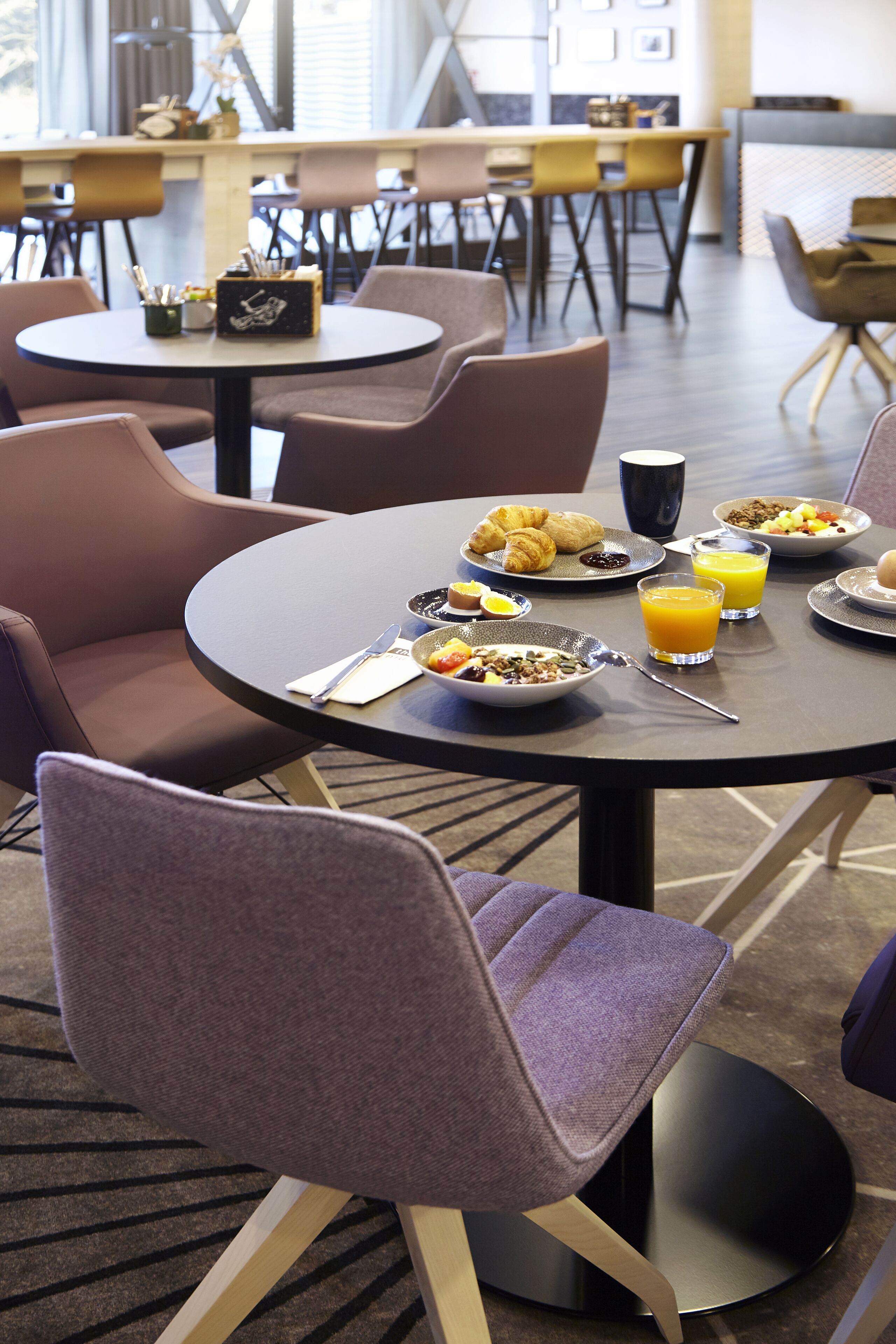 A breakfast setting with round tables, chairs, and a variety of breakfast items including croissants, eggs, and orange juice.