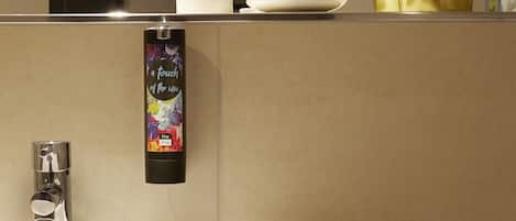 Un bagno con un lavandino bianco, uno specchio, un porta-spazzolini con due spazzolini, una pianta in vaso e un dispenser di sapone.