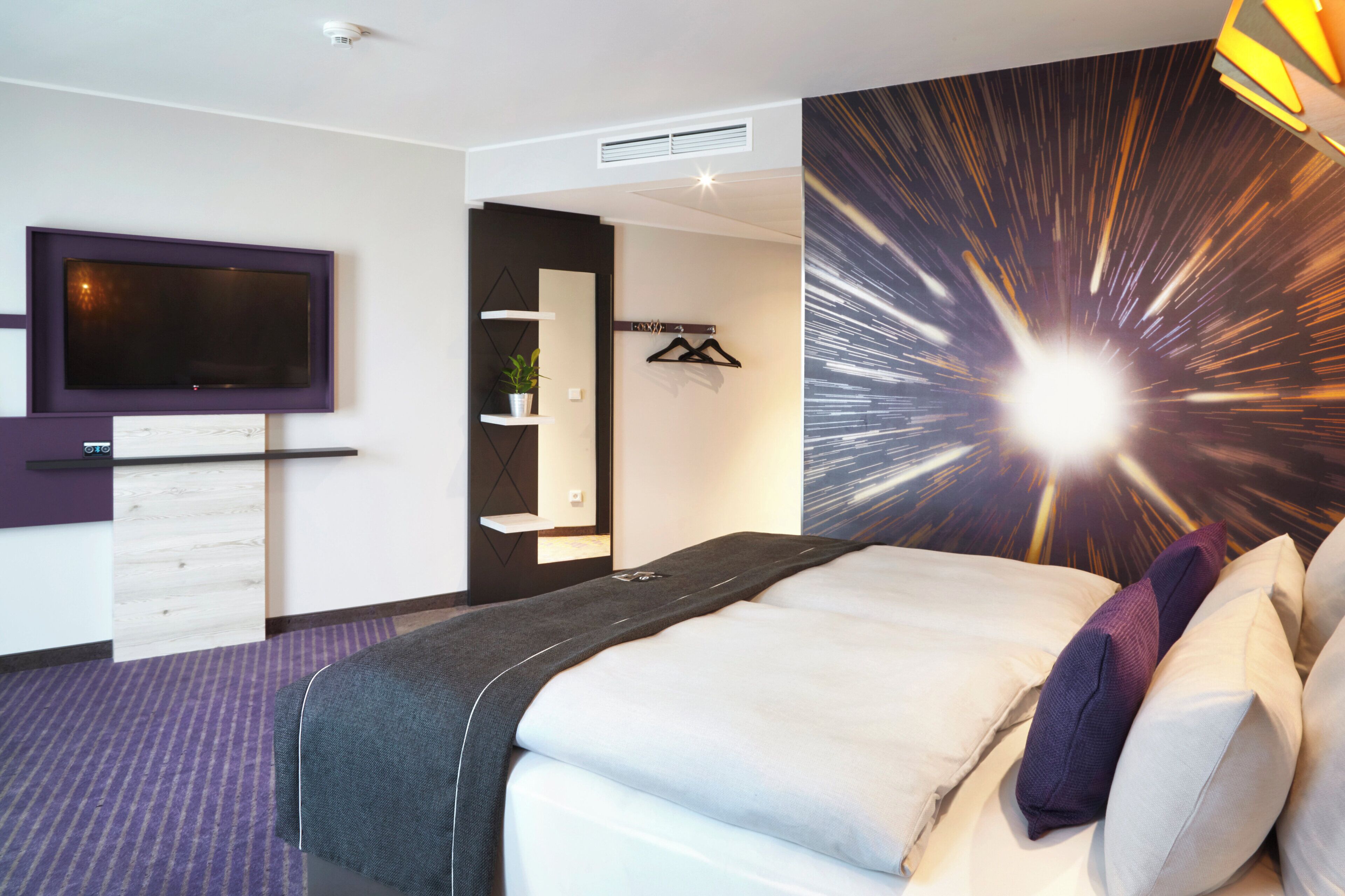 Ein modernes Hotelzimmer mit einem Bett, einem Fernseher, einem Kleiderschrank und einer Wand mit einem dynamischen Lichtmuster.